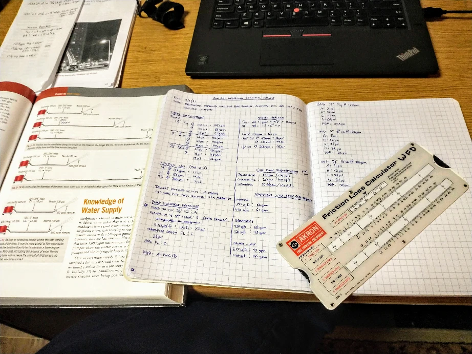 Fire textbook, notebook, and friction loss calculator on a desk.